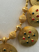 Macro detail of the centerpiece pendant face highlighting the engraved dot-work texture and red and green stone arrangement