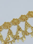 Close-up detail of the repeating open-lattice filigree rosette medallions and diamond-shaped charm drops on swag chains in warm gold-tone