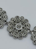 Extreme macro close-up of a single filigree rosette medallion showing the layered open-lattice petal cutwork, beaded border, and clear stone cluster center