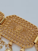 Macro close-up of a single open-lattice filigree rectangular panel showing the raised dome sunburst center motif, rope-twist border, and mixed charm drops