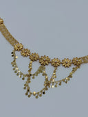 Close-up of the front V-drape showing engraved daisy flower medallions with white bead centers and cascading swag chains of flat round coin disc drops