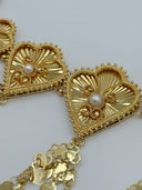 Macro close-up of two heart-shaped fan medallions showing the radial sunburst engraving, beaded border detail, white bead center, and coin disc drop chain attachments