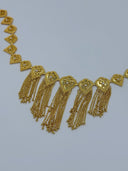 Close-up of the front V-drape showing open-lattice filigree heart medallions with scrollwork bodies, white bead centers, beaded borders, and multi-strand chain tassels with ball tips