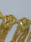 Macro close-up of two filigree heart medallions showing the open-lattice scrollwork body, beaded border, white bead center, and multi-strand chain tassel attachment points