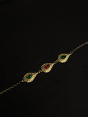 Gold bracelet with green and red gemstones on a black background