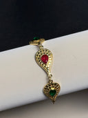 Gold bracelet with red and green gemstones on a mannequin arm.