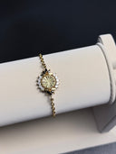 Gold bracelet with a decorative clasp on a white stand against a dark background