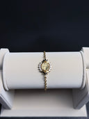 Gold bracelet with a decorative clasp on a white stand against a dark background