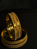 Two gold bangles with intricate designs on a dark background