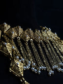 Macro detail of the gold-tone diamond tile choker showing engraved geometric texture, pearl-like bead centres, and multi-chain tassel fringe