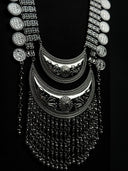 Close-up of layered crescent pendant with floral and dotted relief detailing, central medallion, and dense chain tassel fringe in silver tone