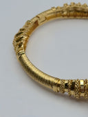 Macro detail of fine wire-wrap ribbed band and granulated disc rings on gold-tone open-cuff bangle