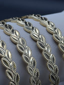Close-up flat lay of four gold-tone Laurea bangles showing the granulated beaded leaf outlines and interlocking diagonal wheat leaf pattern
