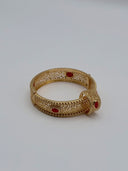 Gold-tone wide hinged bangle with open arabesque filigree body, beaded borders, and oval red stone cabochons, styled on a white surface with a matching ring