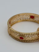 Close-up top view of the Andalus hinged bangle showing the open-lace arabesque filigree pattern and oval red stone cabochons with beaded frames