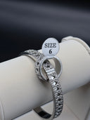 Silver-tone Cannage quilted cuff bangle and matching wide-band ring shown together on a white jewelry display roll, size 6 tag visible