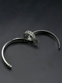 Flat lay of the Cannage open-cuff bangle and quilted ring on a dark surface, showing the open cuff construction, clasp detail, and diamond lattice texture