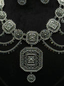 Detail flat lay of the Turath necklace showing the large square centrepiece pendant with layered filigree frames, alternating medallions, and flat coin disc swag drops