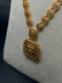 Close-up of the long necklace pendant showing intricate filigree engraving and beaded border detailing on the rectangular drop