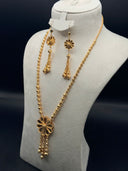 Full view of a 3-piece gold-tone jewelry set on a bust display, showing a long textured bead chain with a large flower pendant and tassel drop, and matching drop earrings