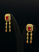 Drop earrings featuring an octagonal ruby-red centre stone with double-halo detailing and dual tassel chains ending in coloured stone drops, displayed on a black velvet stand