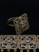 Close-up of a gold-tone cocktail ring with a large square pavé face featuring a four-pointed star centre motif and marquise-cut stone accents, with the choker visible below