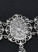 Macro detail of a single oval filigree medallion from the choker, highlighting the geometric and botanical openwork pattern inside the scalloped silver-tone frame