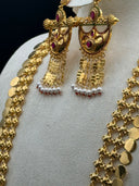 Close-up of the crescent half-moon pendant featuring intricate engraved floral and paisley motifs, ruby-red and emerald-green kundan stones, and cascading gold bar tassels with white pearl drops