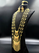 Two layered gold-tone crescent necklaces with open filigree scrollwork, pink and white stone clusters, and cascading capsule-and-ball tassel drops, displayed flat on a dark surface