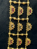 Detail shot of a large crescent necklace pendant with dense open filigree scrollwork, pink and white stone clusters, and rows of capsule tassel drops, photographed on a dark velvet surface