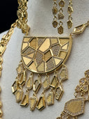 Detail shot of the half-moon pendant face showing the geometric mosaic pattern of pave stone and ridged gold-tone triangular and angular sections, with kite and coffin-shaped charm drops below