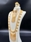 Full view of a Khaleeji-style gold-tone bridal set on a white bust against a dark background, showing a double crescent pendant necklace with chain tassel fringe, two long coin chain side strands with round medallion discs, and matching chandelier earrings