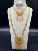 Full view of a Moroccan-style gold-tone jewelry set on a white bust against a dark background, showing a shorter crescent pendant necklace layered over a long opera-length necklace on engraved diamond-station chains, with matching drop earrings