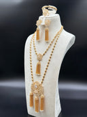 Full view of a Rajwadi-style gold-tone set on a white bust showing two long engraved oval bead chain necklaces with lotus pendants and chain tassel drops, matching chandelier earrings, bracelet, and cocktail ring against a dark background