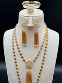 Three-quarter view of the full set on a white bust showing the layered engraved oval bead chains, lotus pendants with chain tassels, chandelier earrings, and the bracelet and ring displayed at the top against a dark background