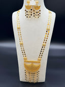 Full front view of a Khaleeji-style gold-tone set on a white bust against a dark background, showing a long two-strand diamond-link necklace with a large open lattice mesh crescent pendant and dense clover-and-diamond tassel fringe, with matching chandelier earrings above