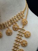 Detail shot of the large oval filigree pendant face showing the open scrolling vine motifs, stone-set floral clusters throughout, scalloped border, and the dense rectangular fringe of stone-set clover chain drops below