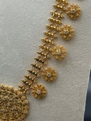 Detail of the coin disc chain side strand showing engraved round discs with floral center motifs and beaded borders hanging from the diamond-link clover chain, with the edge of the large oval filigree pendant visible at bottom left