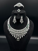 Full view of the 4-piece silver-tone green and clear zirconia set on a black bust, showing the bib necklace, tiara headpiece, chandelier earrings, and cocktail ring