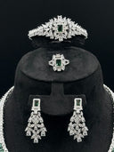 Detail view of the tiara headpiece with green rectangular halo centerpiece and marquise stone rays, alongside the cocktail ring and chandelier earrings