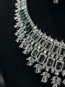Side detail of the bib necklace showing the graduated green rectangular halo rows, marquise clear stone accents, and leaf spray drops along the hem