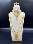 Full jewelry set on a white velvet bust — long double-strand clover link necklace with filigree daisy stations, tassel drop earrings, cuff bracelet, and triangle cord pendant necklace