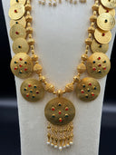 Close-up of the large oval centerpiece pendant showing engraved scrollwork, scattered red and green stones, and multi-strand teardrop and pearl-tipped tassel fringe
